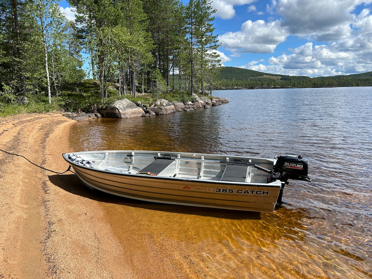 Aluminiumsbåt med motor ved strandkanten.